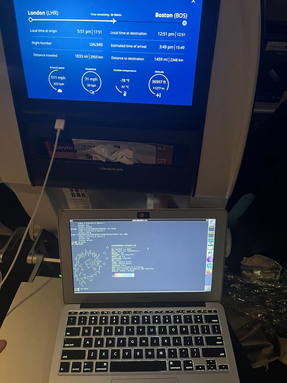 OpenBSD on a 2013 Macbook Air sitting on an airplane tray table showing the output of neofetch in an xterm window, flight status in seatback above shows altitude of 36997 ft and speed of 551 mph