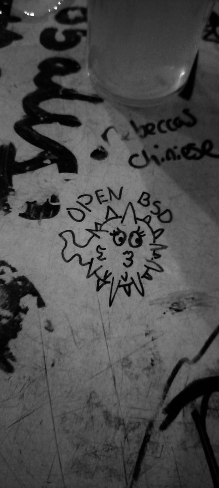 A grayscale photo of some OpenBSD graffiti on a pub table