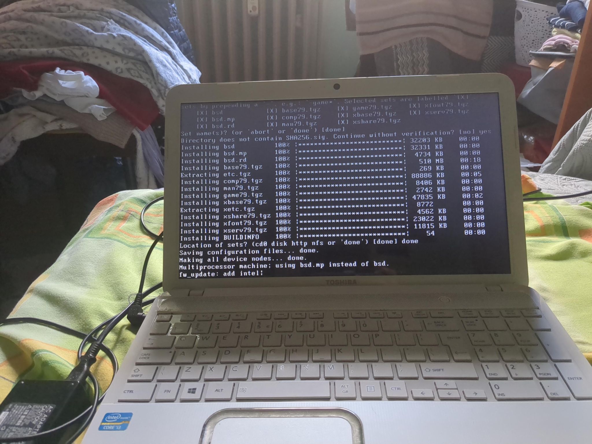 Toshiba laptop running OpenBSD installer, on a bed with green cover.
